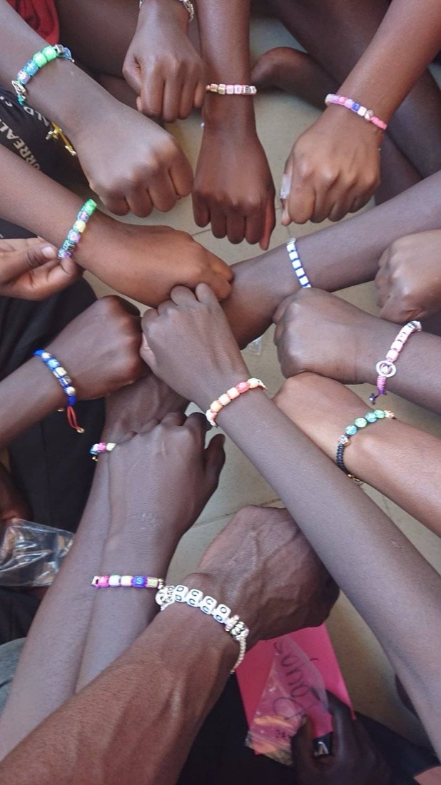 A circle of children&rsquo;s arms reaching into the middle, each wrist wearing a beaded friendship bracelet